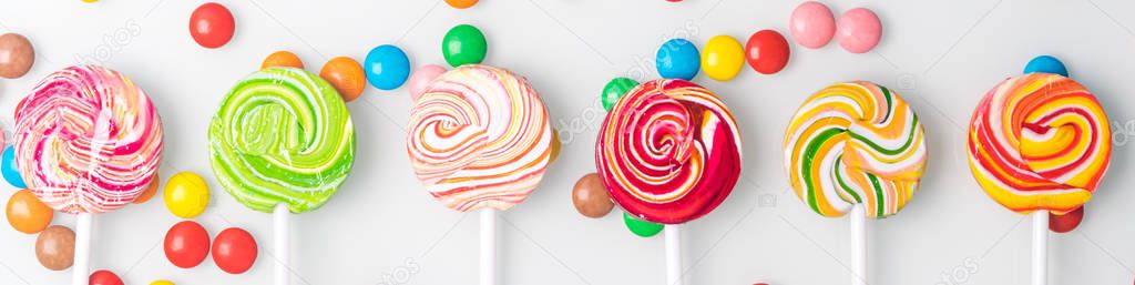 concept of caramel colored lollipops and chocolate dragees on a light background, long photo