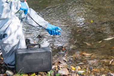 Koruyucu giysi uzmanı, göletteki aleti ölçüyor, yakın plan.