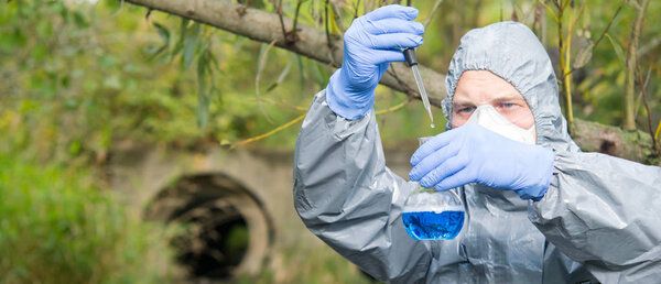 scientist in a protective suit and mask, collects a sample of water in a flask with a blue liquid, close-up, there is a place for the inscription
