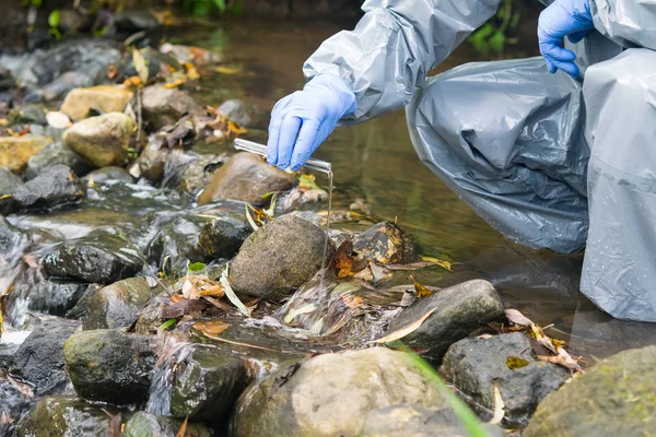a man in a protective suit stands in a river and pours water from a test tube into it with a reagent to analyze the level of pollution