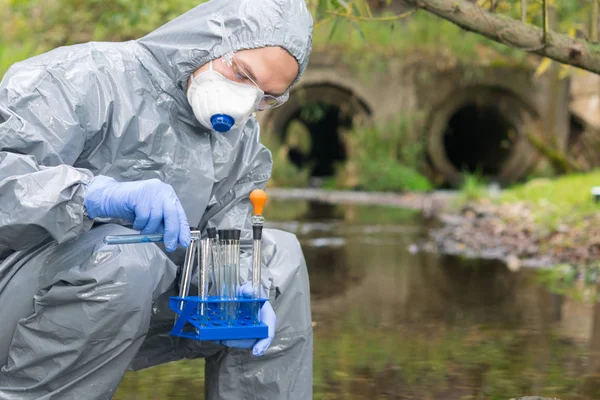 employee in a protective suit and mask conducts a rapid test of water from a river using a mobile laboratory