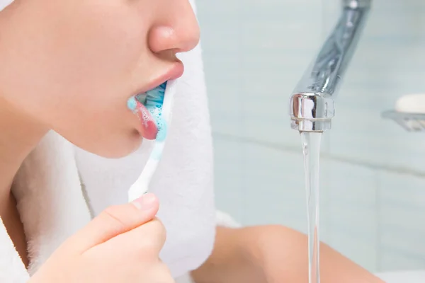 close-up, girl in a white coat, brushing his teeth in the bathroom, near the tap