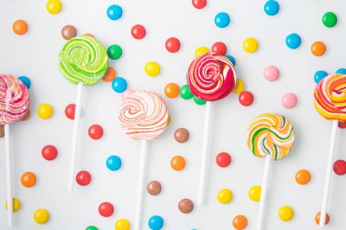 Çok renkli tatlı lolipoplar, beyaz bir arka planda düzgünce serilmiş ve yuvarlak cereyanlar.