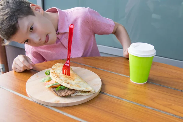 少年はテーブルに座って食欲を持ってバーガーを見て — ストック写真
