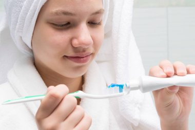 Kafasında beyaz havlu olan kız diş fırçasına yapıştırıcı sürmüş.