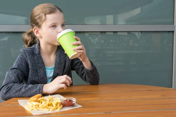 Chica Bebe Una Bebida Come Papas Fritas Sentado Una Mesa — Foto de Stock