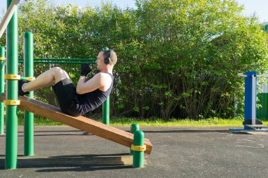 Spor sahasında bir adam basın üzerinde egzersiz yapıyor ve kulaklıkla müzik dinliyor.