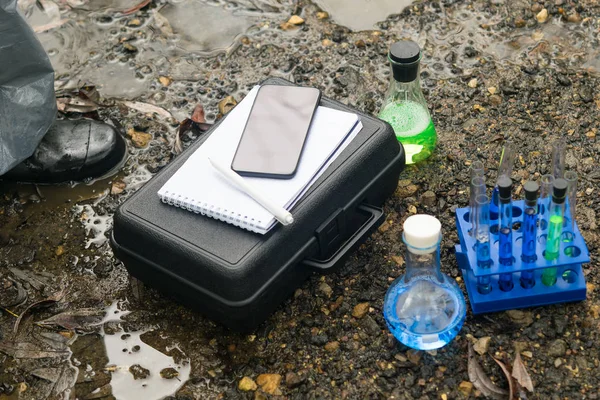 case with tools and instruments for checking the environmental friendliness of the environment next to flasks and test tubes with reagents for soil and water research