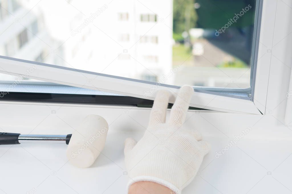 window installation worker inserts glass into the frame and fastens it with a rubber mallet, rear view, close-up