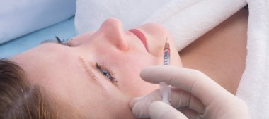 Kozmetoloji, steril eldivenli eller bir kadına çenesinden güzellik iğnesi yapar.