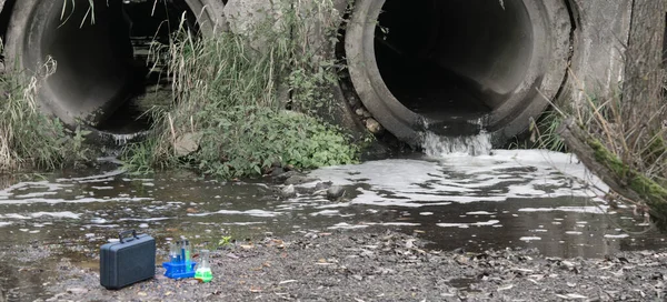 on the background of drainpipes, there are test tubes with liquids and a suitcase for testing in the laboratory