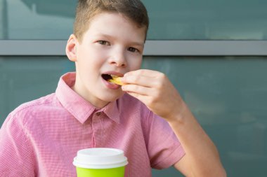 Sıcak çay içip patates kızartması yiyen bir çocuğun ön görüntüsü.