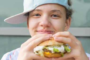 Elinde kocaman bir hamburger tutan ve gülümseyen bir kız.