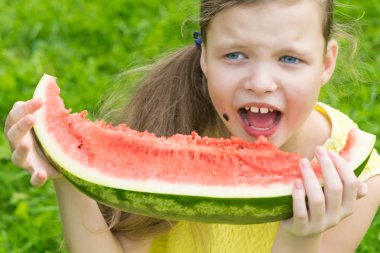 Kirli yüzlü mutlu kız sokakta olgun kırmızı bir karpuz yiyor.