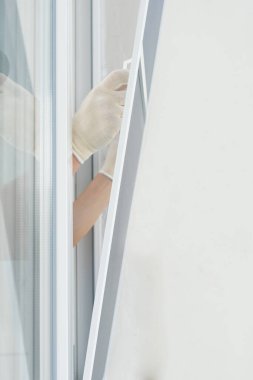 Beyaz eldivenli ustalar plastik pencereye cibinlik takar.