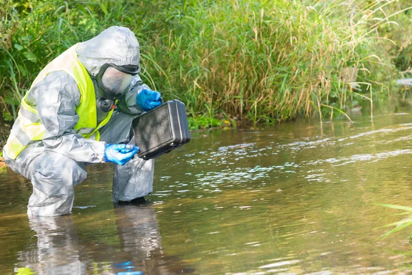 an environmental laboratory specialist in a protective suit and mask stands in the water and measures the level of pollution with the device