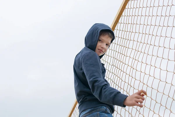 a boy in a hood climbed a fence from a net, street children