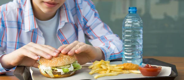 テーブルに座っているシャツの女の子のクローズアップは ファーストフード バーガー フライドポテトを食べています — ストック写真