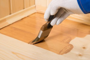 Fırçalı el, ahşap zemini koyu cila ile kaplar.