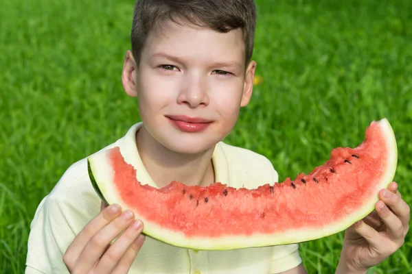 Pohledný Chlapec Jíst Velký Plátek Červeného Melounu Pozadí Zelené Trávy — Stock fotografie