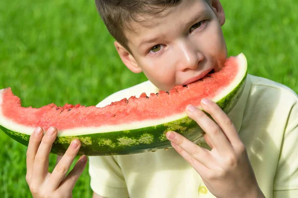 Vacker Pojke Biter Stor Bit Röd Vattenmelon Bakgrund Grönt Gräs — Stockfoto