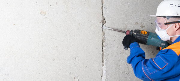 cleaning the walls of old concrete, for applying new plaster, using a drill, a worker in protective clothing, glasses and a hard hat, there is a place for the inscription