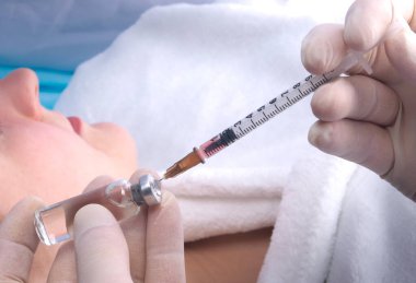 Koruyucu eldivenli bir doktor, beyaz önlüklü bir hastanın geçmişine karşı şırınga ya da iğne için ilaç kullanıyor.