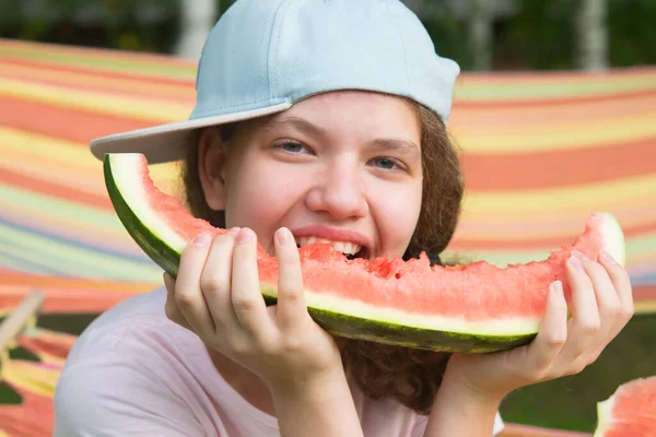 キャップの中で陽気な女の子がスイカを食べ屋外で — ストック写真