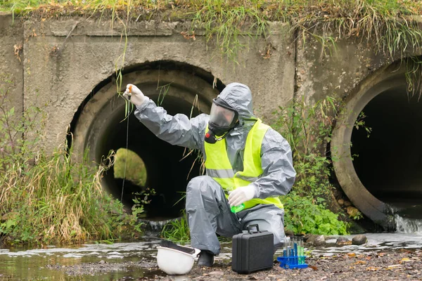 a man in a protective suit and mask from bacteria and viruses drops reagent from a pipette into the river water during an express analysis for contamination