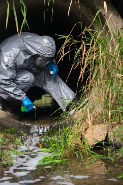 a man in a protective suit and mask in a large sewer pours reagent from a flask for wastewater treatment