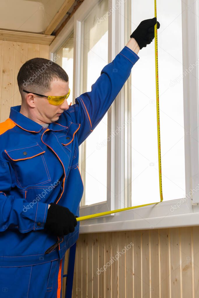 Side view of a man in construction clothing measuring a window opening with a tape measure