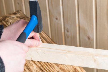 Tahta bir yüzeyi onarmak için çivi tutan bir elin yakın çekimi.