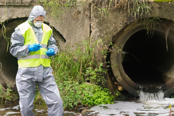 a man in a protective suit takes soil samples into a Petri dish from the sewage treatment plant