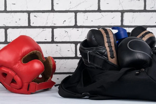 ブラックスポーツバッグに訓練用のものとレンガの壁の背景に赤い保護ボクシングヘルメット — ストック写真