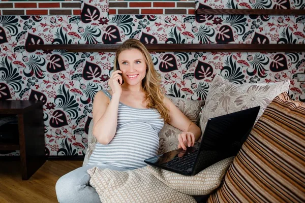 Koltukta dinleniyor, telefonda konuşurken ve dizüstü bilgisayarda çalışan hamile kadın.