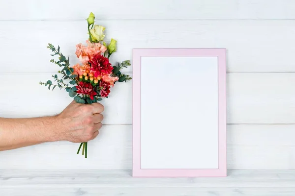 Çiçek ve bir fotoğraf çerçevesi ahşap arka plan üzerinde tutan adamın el.