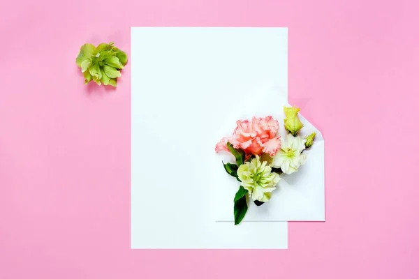Kleurrijke Lentebloemen in envelop en wit blad op roze achtergrond. — Stockfoto