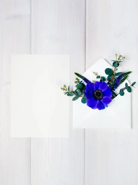 Цветные весенние цветы в конверте и белый лист на деревянном фоне . — стоковое фото