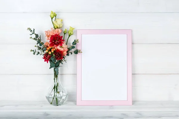 Çiçek vazo ve ahşap arka plan üzerinde bir fotoğraf çerçevesi.
