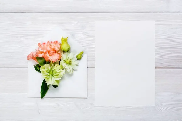 Барвисті весняні квіти в конверті і білий аркуш на дерев'яному фоні . — стокове фото
