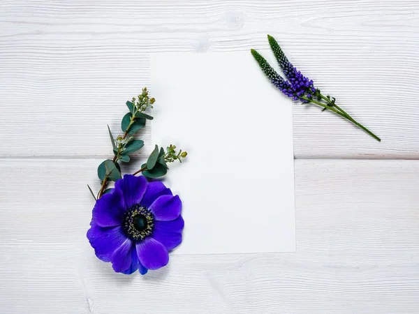 Mavi çiçekler ve ahşap arka plan üzerinde beyaz sayfa.