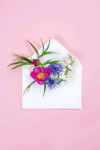 Kleurrijke zomerbloemen in envelop op roze achtergrond. — Stockfoto