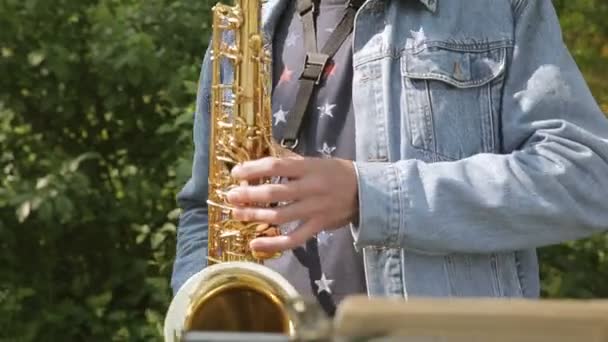 Saxofoon in de handen van straatmuzikanten in de denim jasje met akkoorden — Stockvideo