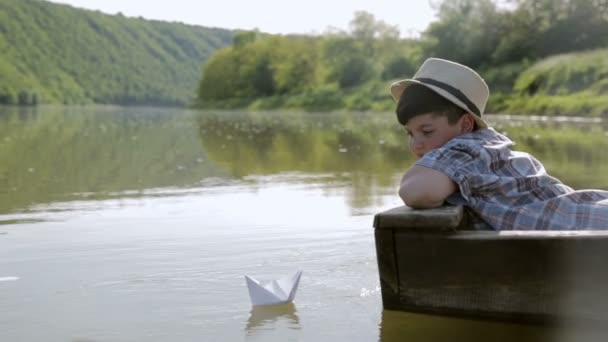 El chico pone un barco de papel en el agua y deja que la vela — Vídeos de Stock