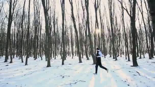 Un joven corredor corre en el frío bosque invernal matutino. Atleta durante el entrenamiento. Bosque denso — Vídeos de Stock