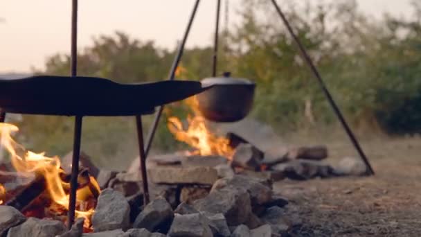 MOZIONE DOLLY: Cucinare due piatti in fiamme. Cibo nella campagna. Viaggio nelle foreste selvagge per la fauna selvatica. Viaggi romantici. Abbigliamento da viaggio. Pentole turistiche in fiamme. Rivestito fuoco di pietra — Video Stock