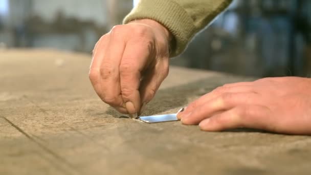 Close-up hand of a young blacksmith who draws a chalk line on the table with a metal ruler. — Stock Video