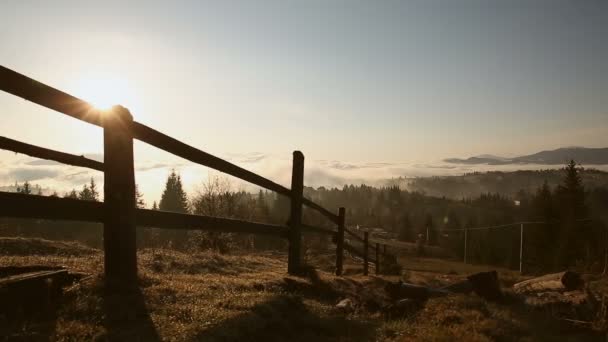 Солнце светит через деревянный забор в горах. Красивые горы, покрытые туманом. Восток или запад в горах — стоковое видео