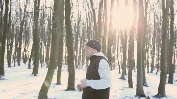 Hombre corriendo en el parque de invierno en los auriculares. Entrenamiento al aire libre al atardecer — Vídeos de Stock