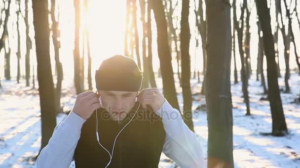 Joven corredor con auriculares en el parque al atardecer. Entrenamiento de invierno para la recuperación — Vídeos de Stock